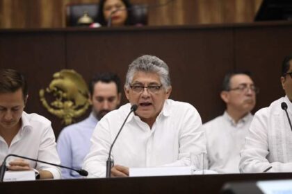 Hombre hablando por micrófono con guayabera en una sesión del Congreso